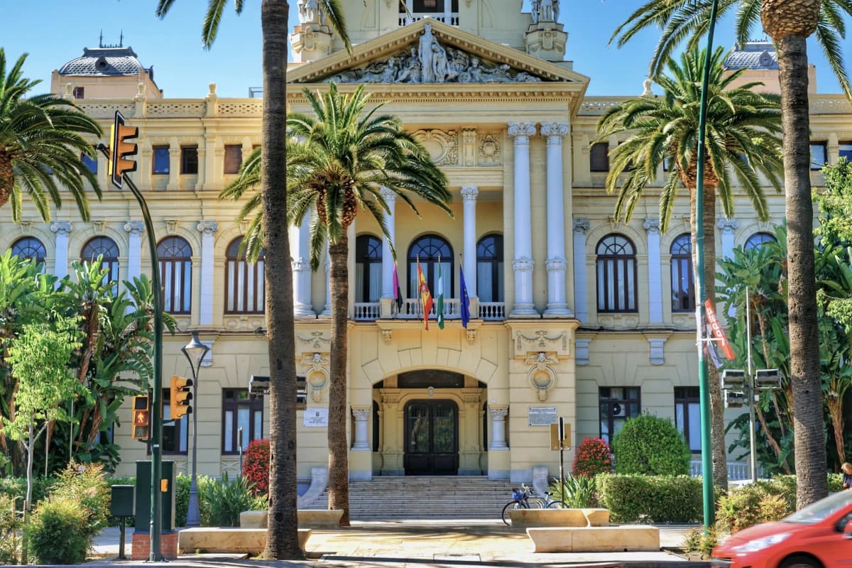 A picturesque view of Malaga's old town with historic buildings and palm trees along the waterfront, reflected in the calm blue sea.