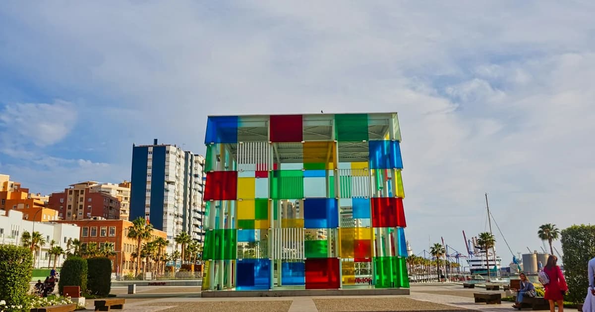 Centre Pompidou Malaga: Colourful glass cube museum on waterfront with red, green, blue panels, skyline, marina, palms.