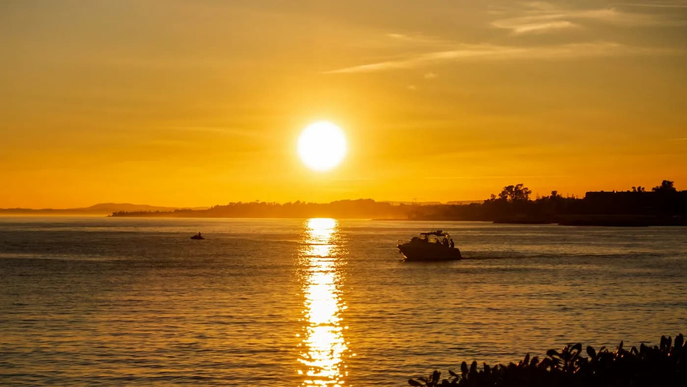 Sunset over the sea in Marbella, with golden sky reflections on the water and a motorboat cruising near the shore.