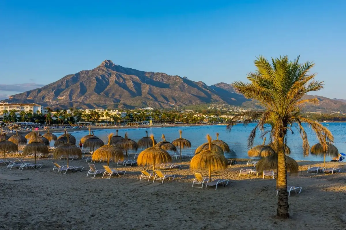 Beautiful Marbella beach with golden umbrellas, sun loungers, palm trees and stunning La Concha mountain backdrop on Costa del Sol