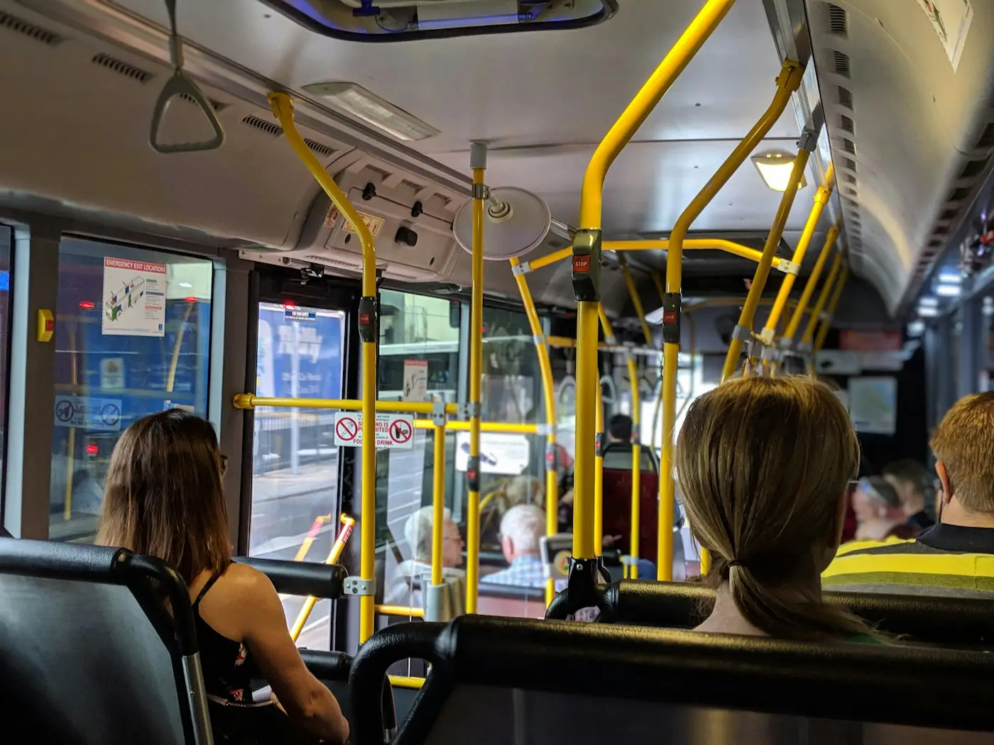 Interior of an EMT bus in Malaga with yellow handrails, passengers seated, and a view of city streets through the window.