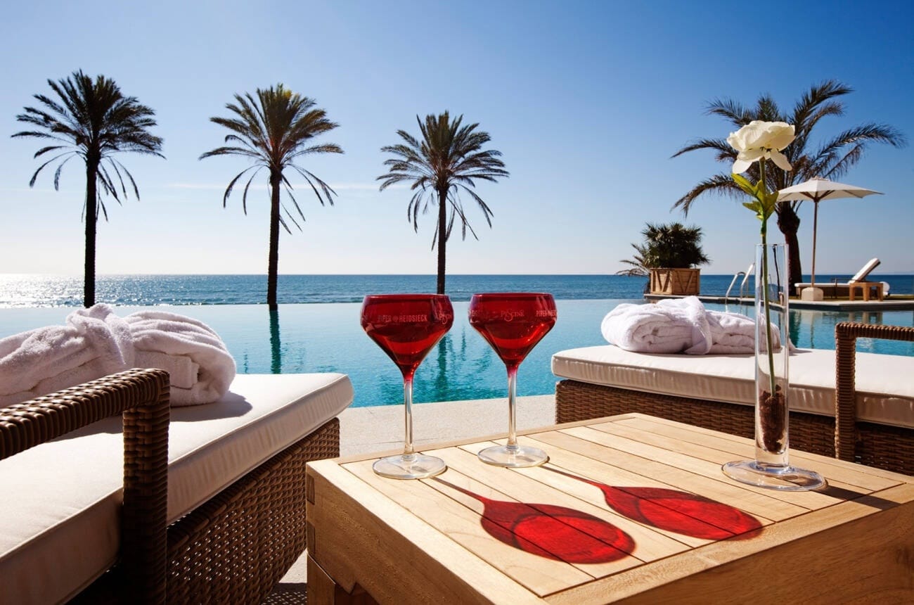 Luxury beach club pool in Marbella, Malaga, Andalusia, Spain with infinity pool, palm trees, sun loungers and drinks overlooking the sea