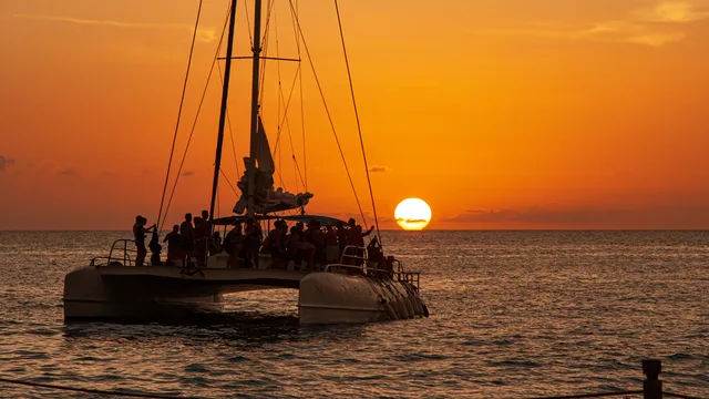 Silhouette of a catamaran packed with passengers sailing into a vivid orange sunset off the Málaga coast