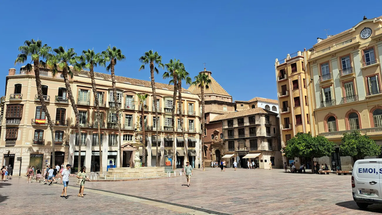 Malaga city center with palm trees, historic buildings, and pedestrians in a sunny plaza