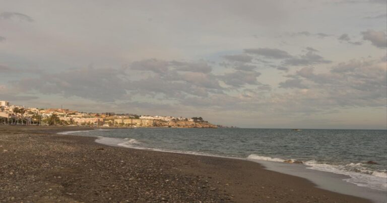 Cloudy winter beach in Malaga, Spain, with calm waves and coastal city view – typical January weather on the Costa del Sol.